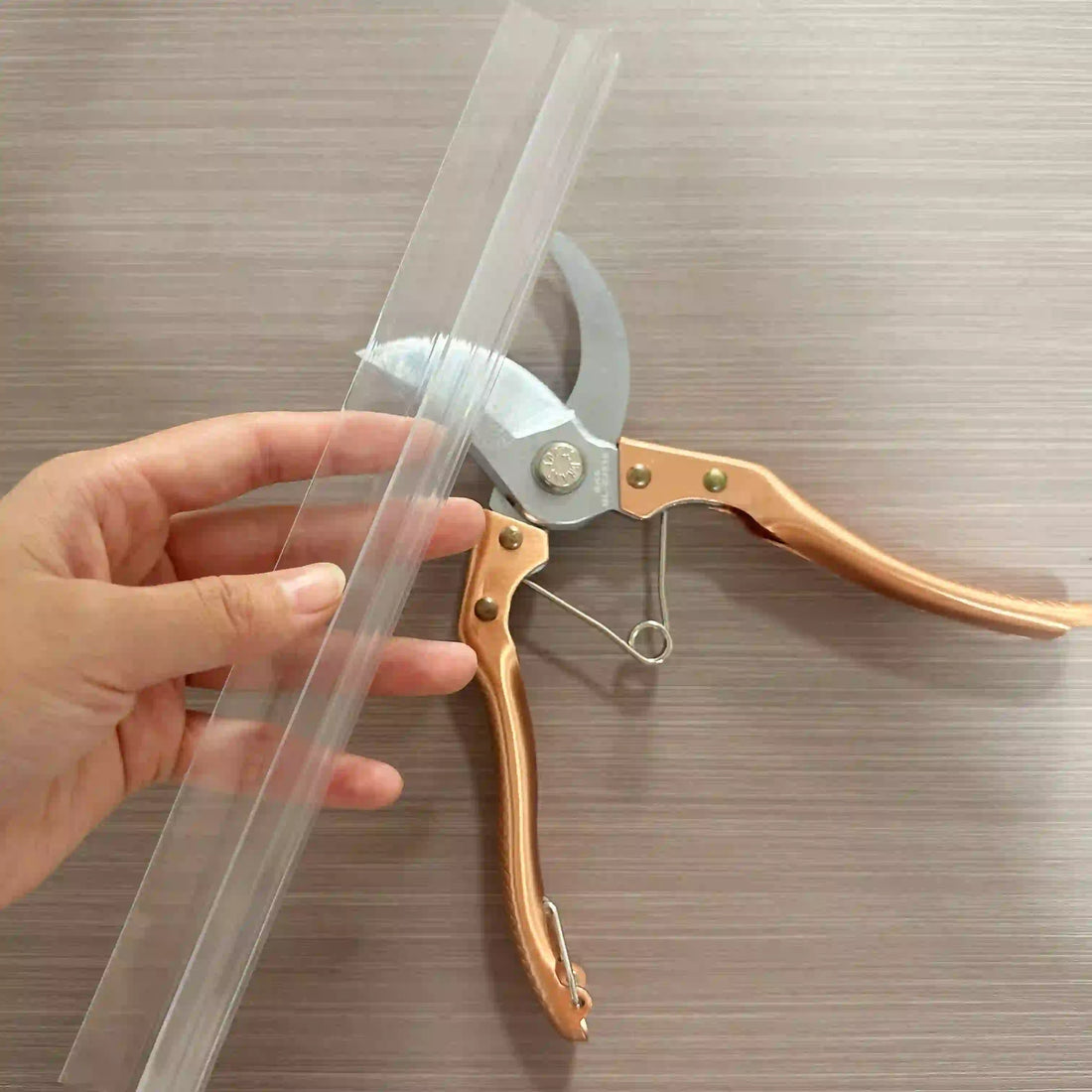 Using garden pruners to cut a white silicone shower door seal, ensuring straight edge for waterproofing