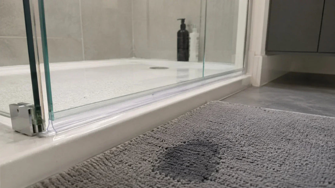 Frameless shower door with a clear bottom seal rubbing slightly against the tray and a damp bath mat outside