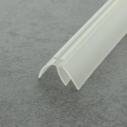 High-clarity close-up of a framed shower door bottom seal strip (clear version), showcasing the high light transmission, smooth vinyl texture, and exceptional flexibility of the VE02's complex triple-fin structure, highlighting its resistance to ageing as an effective substitute for failed old seals to provide a triple waterproof barrier while remaining virtually invisible beneath the glass door to maintain bathroom aesthetics.