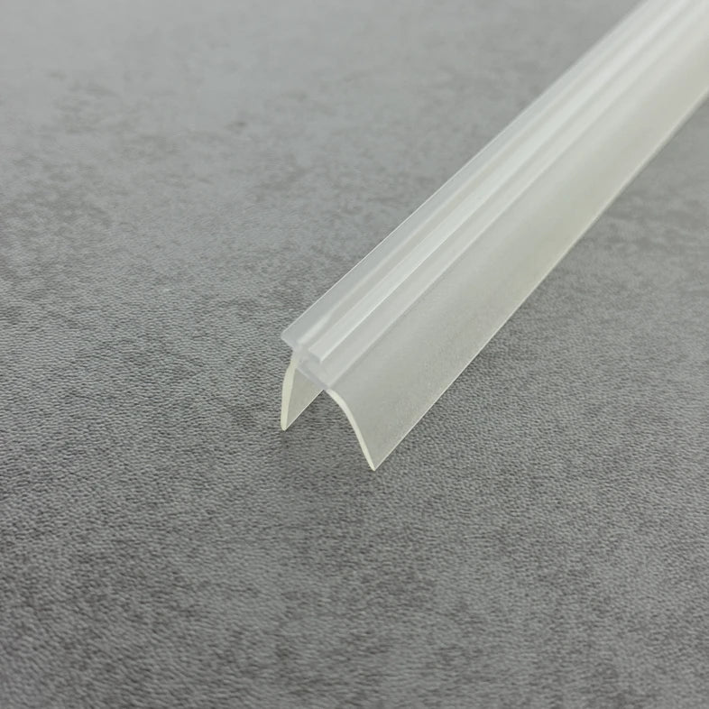 High-clarity close-up of a shower door frame gasket (clear version), showcasing the high light transmission, smooth vinyl texture, and flexibility of the VE01's complex profile (including the side rail), highlighting its resistance to ageing as an effective substitute for hardened or failed old gaskets to provide dual-layer protection while remaining virtually invisible beneath the glass door.
