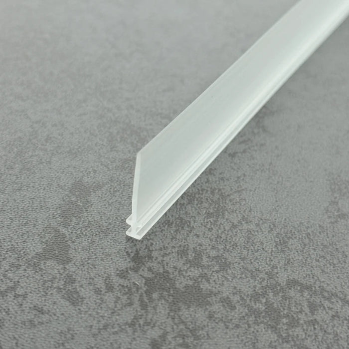 High-clarity close-up of a framed shower door bottom seal replacement (clear version), showcasing the high light transmission, smooth vinyl texture, and flexibility of the VI004's 15mm fin, highlighting its resistance to ageing as an invisible solution to restore waterproofing at the base of framed doors.