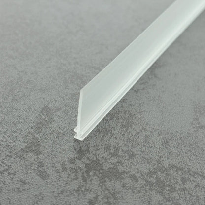 High-clarity close-up of a framed shower door bottom seal replacement (clear version), showcasing the high light transmission, smooth vinyl texture, and flexibility of the VI004's 15mm fin, highlighting its resistance to ageing as an invisible solution to restore waterproofing at the base of framed doors.