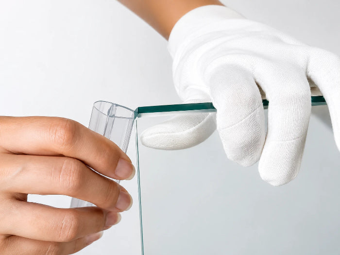 Hand fitting a clear shower door seal onto a glass shower screen